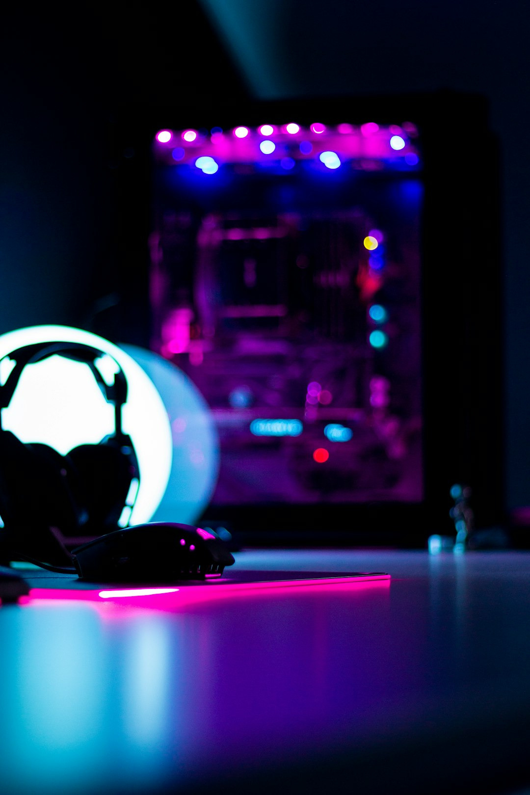 Gaming mouse and headphones near a glowing PC tower.